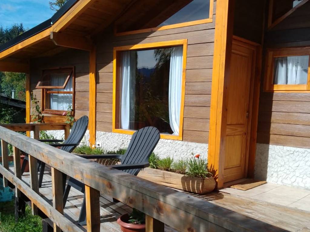 Deck de madera con sillas al sol frente a una cabaña