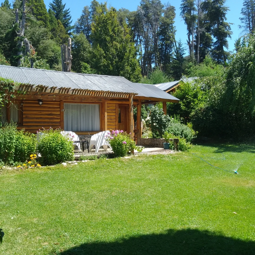 Cabaña de troncos rodeada de césped y canteros en verano
